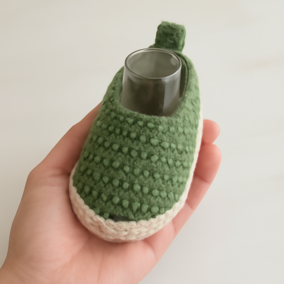 Crochet cute baby shoes in muted green and creamy beige colors with a rounded toe box and cuffed heel, placed on a light background.