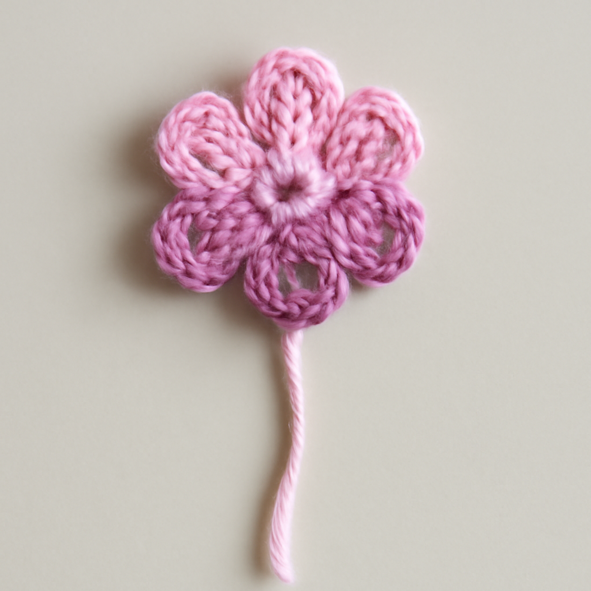 A set of crocheted flowers in light pink, dark pink, lavender, and purple showcasing six petals, created using shell stitch, single crochet, and double crochet techniques.