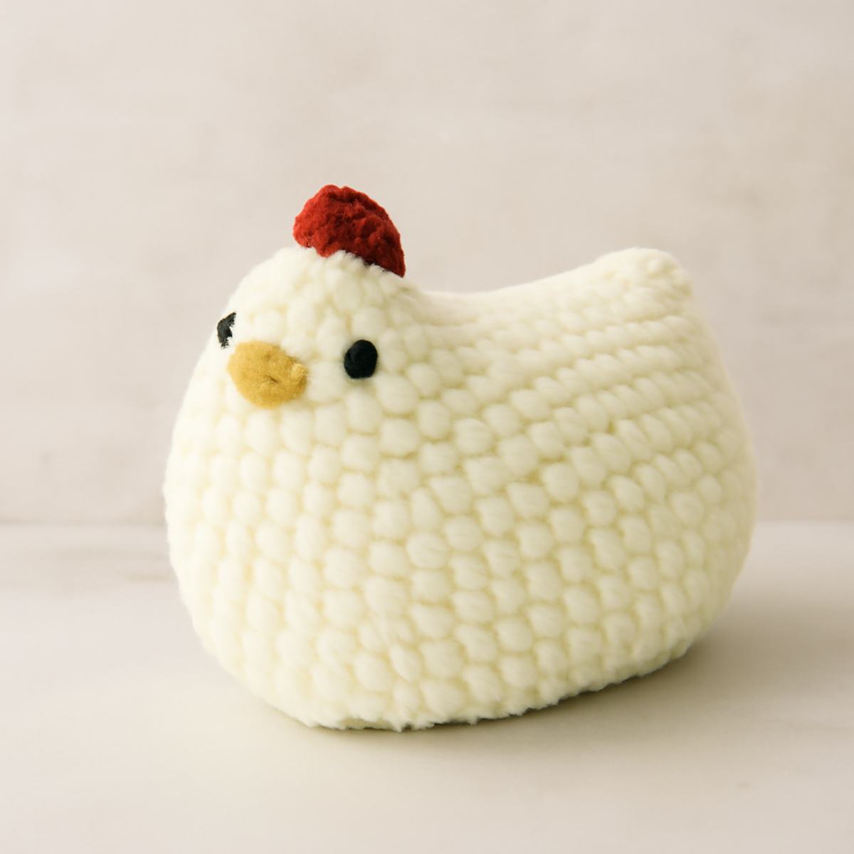 A soft, plush crochet chicken with a red comb, tan beak, and black safety eyes, approximately 10-12 inches long and 6-8 inches high.